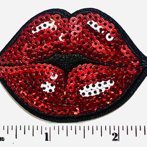 May include: A red sequined lips patch with a black border. The lips are made of shiny red sequins, with white sequins for the teeth. The patch is approximately 2 inches wide.