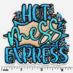 May include: Embroidered patch with the words "HOT MESS EXPRESS" in turquoise and blue lettering. The patch has a tan background and is outlined in black. Brown and blue floral accents surround the text. The patch measures approximately 3 inches wide.
