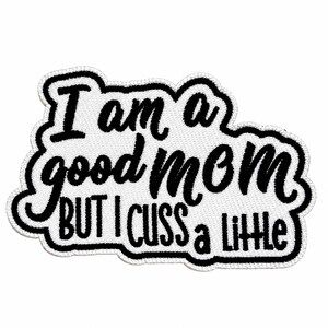 May include: A white embroidered patch with a black stitched border featuring the black text "I am a good mom BUT I CUSS a little" in a combination of cursive and block lettering. The patch has a textured fabric surface and irregular shape.