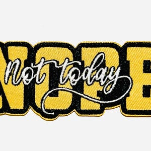 May include: A rectangular patch with the word "NOPE" in large, yellow, embroidered letters with a black border. The words "not today" are written in white script across the center. The patch is approximately 2 inches long.