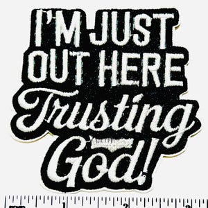 May include: Black and white embroidered patch with the text "I'M JUST OUT HERE Trusting God!" in a stylized font. The patch has a black background with white stitching and a decorative border. The patch is approximately 3 inches wide.
