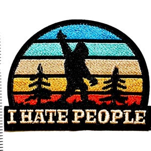 May include: Embroidered patch featuring a Bigfoot silhouette against a sunset backdrop with the text "I HATE PEOPLE." The patch is approximately 2 inches wide and 1.5 inches tall, with a black border and colorful stitching.