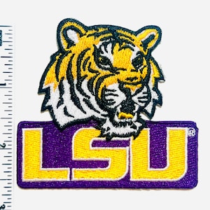 May include: Embroidered patch featuring a tiger head in yellow, black, and white, above a purple rectangle with the yellow letters "LSU". The patch is approximately 2 inches wide and 2 inches tall.