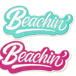 May include: Two embroidered patches with the word "Beachin'" in a cursive script. One patch is turquoise with white lettering, and the other is hot pink with white lettering. Both have a white border.