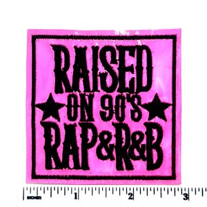 May include: A pink square patch with the words "RAISED ON 90'S RAP & R&B" in black, stylized lettering. Two black stars flank the words "ON 90'S". The patch is approximately 3 inches wide.