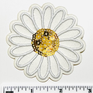 May include: A white daisy-shaped applique with embroidered petals and a gold sequined center. The applique is approximately 2 inches in diameter, perfect for embellishing clothing or accessories.