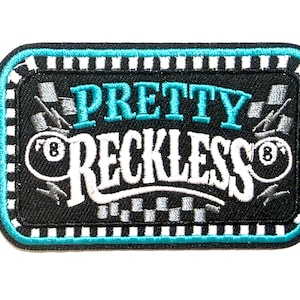 May include: A rectangular patch with the words "PRETTY RECKLESS" in white and teal lettering. The patch has a black background with a teal border and checkered accents. The patch measures approximately 2 inches in height.