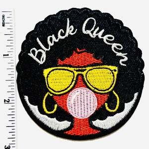 May include: Embroidered patch with a black scalloped border. The patch features a stylized illustration of a person with black hair, yellow sunglasses, and a pink bubble gum bubble. The words "Black Queen" are embroidered in white.