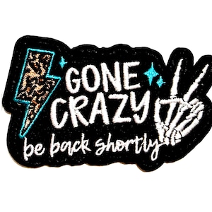 May include: Black patch with white embroidered text reading "GONE CRAZY be back shortly." Features a leopard print lightning bolt and a skeleton hand making a peace sign. The patch measures approximately 3 inches wide.