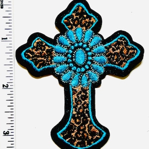 May include: Embroidered cross patch featuring a turquoise floral design at the center, surrounded by a leopard print pattern and outlined in black. The patch measures approximately 3 inches in height.