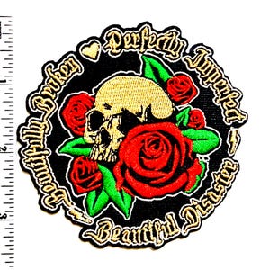 May include: Embroidered patch featuring a skull surrounded by red roses and green leaves. The patch has the words "Beautifully Broken" and "Perfectly Imperfect Beautiful Disaster" in a gold script on a black background. The patch measures approximately 3 inches in diameter.