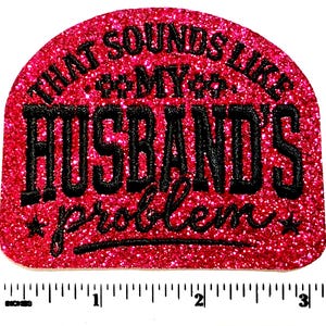 May include: A glittery, semi-circular patch in shades of pink and red. The patch features the phrase "THAT SOUNDS LIKE MY HUSBAND'S problem" in black, stylized lettering. The patch is approximately 3 inches wide.