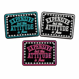 May include: Three rectangular embroidered patches with black backgrounds and white floral borders. Each patch features the text "EXPENSIVE but the ATTITUDE is free" in different thread colors: one in bright blue, one in white, and one in hot pink.