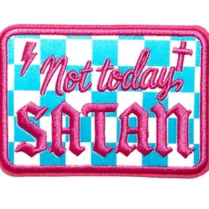 May include: Rectangular patch with a pink border and the words "Not today SATAN" in pink gothic lettering. The background is a checkered pattern of white and light blue squares. A pink lightning bolt and cross are also present.
