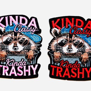 May include: Two embroidered patches featuring a raccoon wearing a blue hat and peeking out of a trash can. The patches have the text "KINDA Classy" and "Kinda TRASHY" in pink and red, with a black border.