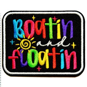 May include: Embroidered patch with the words "Boatin and Floatin" in colorful, rainbow-colored letters on a black background. The patch has a white border and features a yellow sun design.