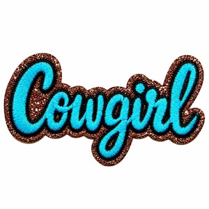 May include: An embroidered patch featuring the word cowgirl in bright blue script lettering. The text is outlined in black thread and set against a shimmering, textured copper-brown glitter background that follows the shape of the letters.