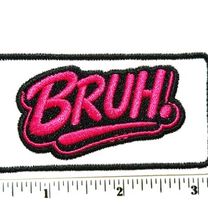 May include: A rectangular embroidered patch featuring the word BRUH! in bright pink thread with a thick black outline, set against a white background. A ruler placed underneath shows the patch is approximately 3.5 inches in total length.