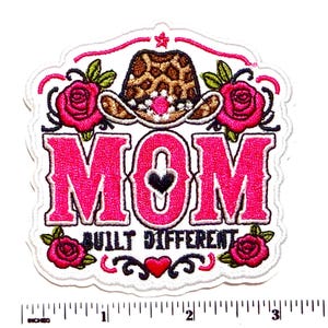 May include: An embroidered patch featuring a leopard print cowboy hat, pink roses, and the text MOM BUILT DIFFERENT with a heart icon. A white ruler at the bottom shows the patch is approximately 3.5 inches wide and 3.5 inches tall.