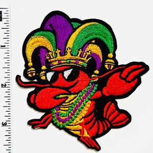 May include: Embroidered patch featuring a red lobster wearing sunglasses, a gold crown, and a jester's hat in purple, green, and yellow. The lobster is adorned with a beaded necklace in matching colors. The patch has a black border.