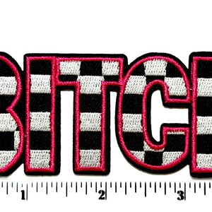 Pu&ograve; includere: Toppa ricamata con la parola "BITCH" a grandi lettere a blocchi. Le lettere sono a scacchi bianchi e neri con un contorno rosa acceso. La toppa &egrave; su sfondo bianco con un righello in pollici.