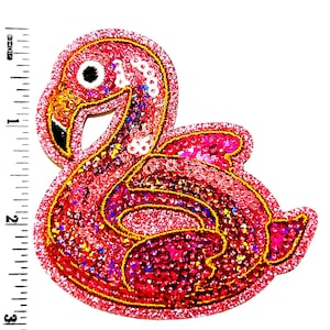 May include: A pink sequined flamingo patch with gold trim. The patch is approximately 3 inches tall. The flamingo has a black beak, a white and black eye, and is covered in pink sequins. The patch is on a white background.