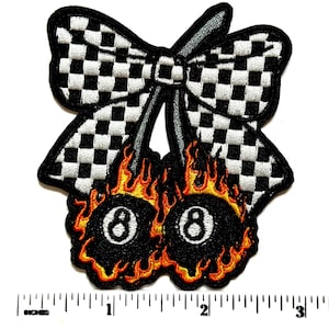 May include: Embroidered patch featuring a black and white checkered bow above two flaming 8-ball designs. The flames are orange and yellow, with the number 8 in white. The patch has a black border.