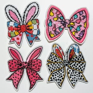 May include: Four embroidered patches in the shape of bows and bunny ears. The bows feature various patterns, including polka dots, floral designs, and bunny prints. Colors include pink, red, blue, yellow, and white. The patches have a white border.