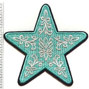 May include: A turquoise star-shaped embroidered patch with white floral designs. The patch has a black border and is approximately 3 inches in height. This decorative patch can be ironed on or sewn onto clothing or accessories.