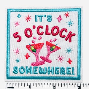 May include: Embroidered patch with a white background, a teal border, and the text "IT'S 5 O'CLOCK SOMEWHERE!" in pink and teal. Two pink martini glasses with green olives are featured. Decorative stars and shapes surround the text.