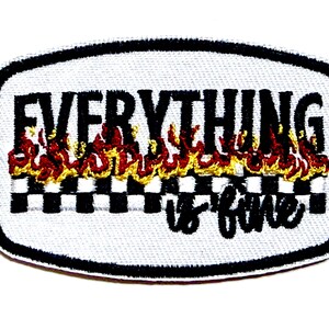 May include: Embroidered patch with the phrase "EVERYTHING is fine" in black script. The text is above a checkered pattern and flames. The patch is approximately 2 inches long and 1 inch tall.