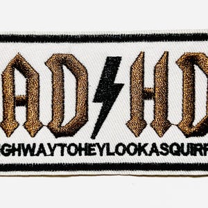 May include: Embroidered patch with the text "AD/HD" in a gothic font, with a black lightning bolt in the center. The phrase "HIGHWAYTOHEYLOOKASQUIRREL" is below the main text. The patch has a black border and is on a white background.