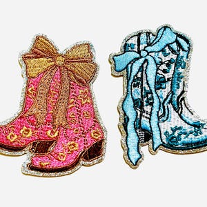 May include: Two embroidered patches of cowboy boots. One pair is pink with gold accents and a gold bow. The other is light blue with a floral design and a blue bow. Both have a silver border.