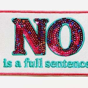 May include: A rectangular patch with a white background and a red border. The word "NO" is embroidered in large, sequined, red letters with teal outlines. Below, the phrase "is a full sentence" is embroidered in teal.