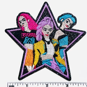 May include: Embroidered patch featuring three stylized figures within a black glitter star. The figures have vibrant hair colors: pink, purple, and blue. The patch includes the word "VODKA" in black letters on a black background. The figures are wearing colorful clothing.
