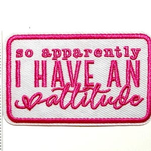 May include: Embroidered patch with the phrase "so apparently I HAVE AN attitude" in pink lettering on a white background. The patch is rectangular with a pink border and measures approximately 2 inches in height.