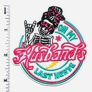 May include: Embroidered patch featuring a skeleton with a rock-and-roll hand gesture, wearing sunglasses and a head wrap. The patch has the text "On My Last Nerve" in a circular design with pink and teal accents. A yellow lightning bolt is also included.