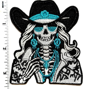 May include: Embroidered patch featuring a skeleton wearing a black cowboy hat with a turquoise band and sunglasses. The skeleton has long white hair and turquoise earrings and necklace. The patch is approximately 3 inches tall.