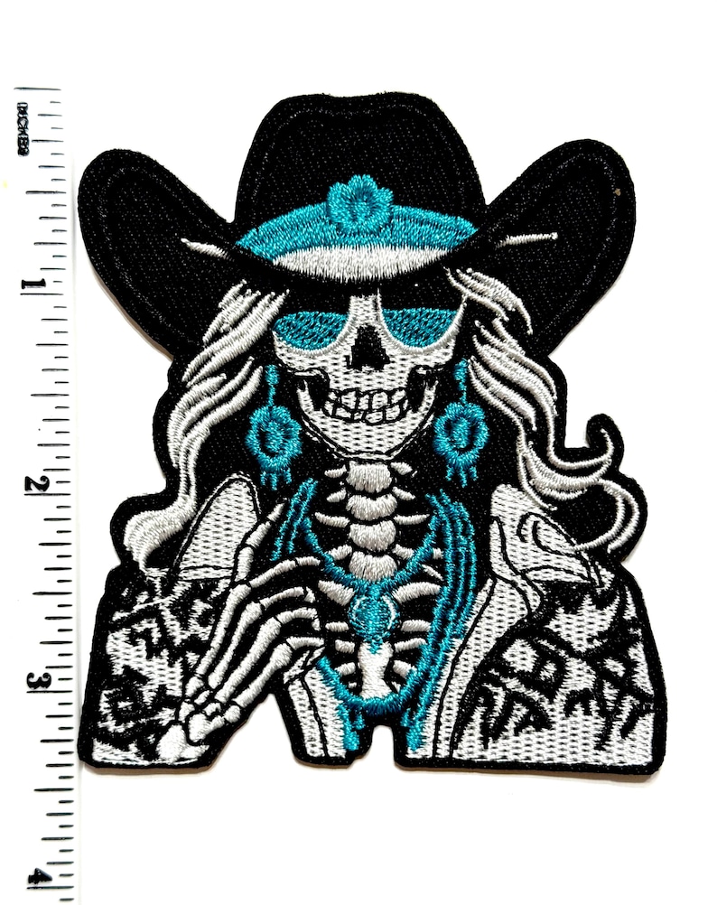 May include: Embroidered patch featuring a skeleton wearing a black cowboy hat with a turquoise band and sunglasses. The skeleton has long white hair and turquoise earrings and necklace. The patch is approximately 3 inches tall.