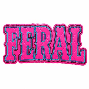 May include: A hot pink quilted patch featuring the word FERAL in bold, block-style lettering. The text is outlined in a bright turquoise blue border, which is further accented by a thin black stitched edge, creating a layered appearance.