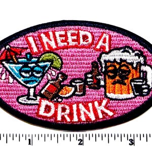 May include: Oval-shaped patch with the text "I NEED A DRINK" in red letters. The patch features cartoon illustrations of a cocktail, bottles, and a beer mug, all with tired expressions. The background is pink.