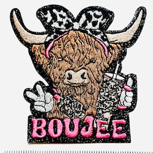 May include: Embroidered patch featuring a Highland cow with a bow, holding a drink, and giving a peace sign. The patch has a black glitter border and the word "BOUJEE" in pink. The cow is brown with a black and white bow.