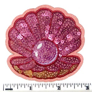 May include: A pink sequined seashell patch with a pearl in the center. The patch has a light pink border and a dark pink embroidered outline. The shell is approximately 3 inches wide.