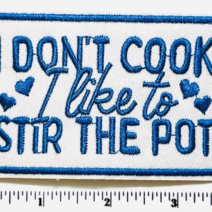 May include: Embroidered patch with the phrase "I DON'T COOK I like to STIR THE POT" in blue script on a white background. The patch has a blue border and blue heart accents.