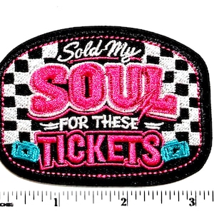 May include: Embroidered patch with the text "Sold My Soul For These Tickets" in pink and white. The patch has a black border and a checkered background. Includes two turquoise ticket graphics.