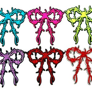 May include: Six embroidered patches shaped like bows made of barbed wire. The colors include bright blue, hot pink, neon yellow, purple, dark red, and a red and white combination. Each bow features a detailed wire texture with sharp spikes.