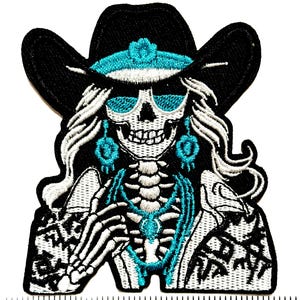May include: Embroidered patch featuring a skeleton wearing a black cowboy hat with turquoise accents and sunglasses. The skeleton has long white hair and turquoise jewelry. The patch has a black and white patterned jacket and a skeleton torso.