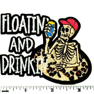 May include: Embroidered patch featuring a skeleton wearing a red baseball cap, holding a blue can, and sitting on a leopard print design. The patch has the words "FLOATING AND DRINKIN" in white block letters with a black border.