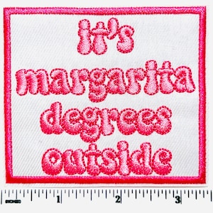 May include: Embroidered patch with a white background and a bright pink border. The patch features the phrase "It's margarita degrees outside" in pink, bubble-style lettering. The patch is rectangular and includes a ruler along the bottom edge.