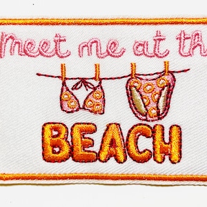 May include: Embroidered patch with the text "Meet me at the BEACH" in orange and pink. The patch features a bikini and bottoms hanging on a clothesline. The patch has an orange border.
